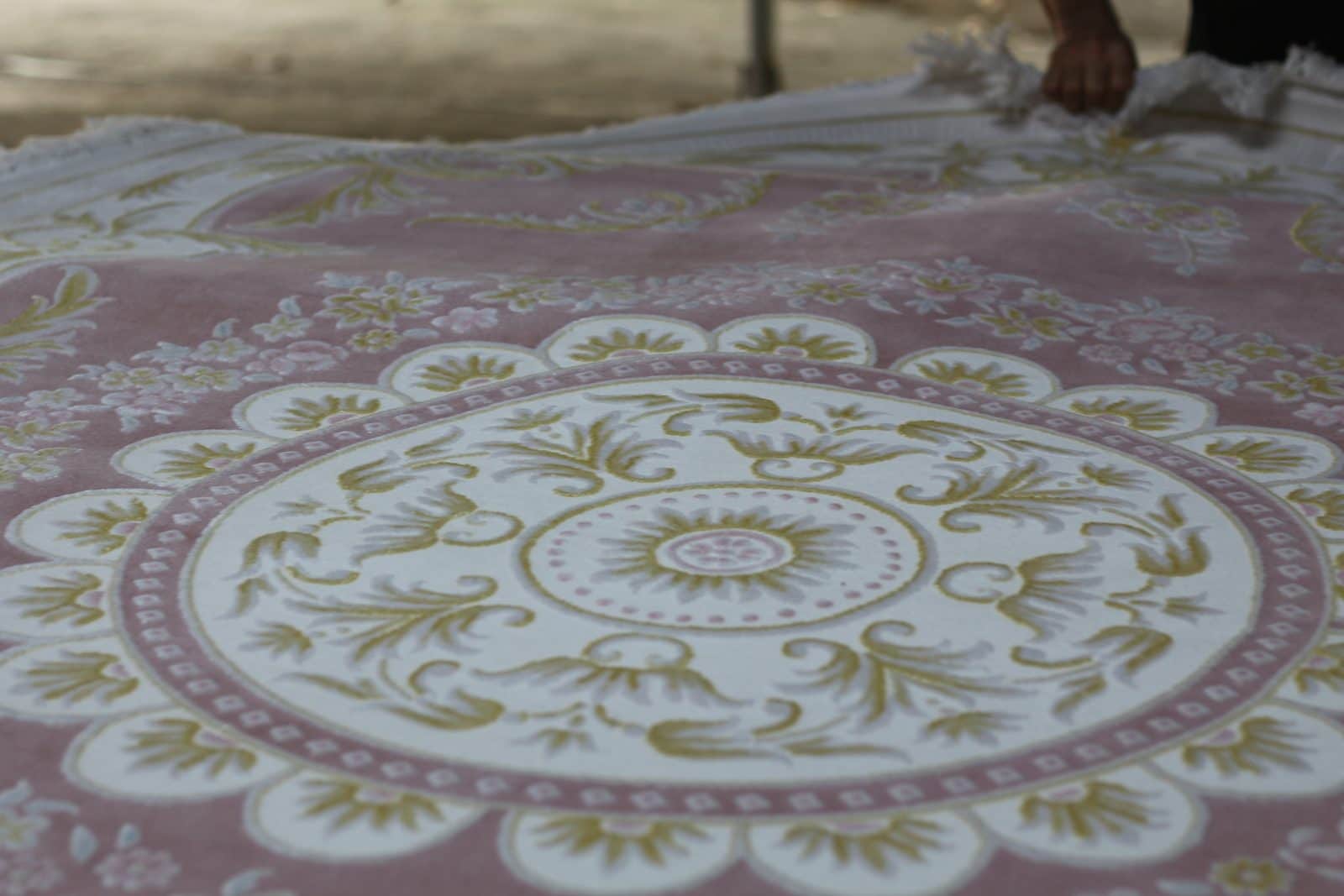 Madalyon desenli pembe bir halı zemine serilmiş, bir çalışan kenarını düzeltiyor